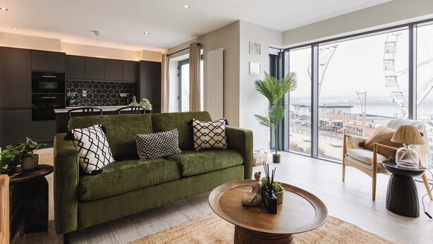 A modern living room with a green sofa, a round coffee table, and a view of a cityscape through large windows.