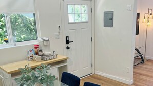 A modern kitchen with a white door, a coffee maker, and a window with greenery outside.