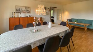 Uma sala de jantar com uma mesa redonda, cadeiras, um lustre e vista para outro espaço com um sofá e um banco.