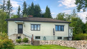 Uma casa de dois andares com escadaria de pedra, um pequeno alpendre e um jardim.