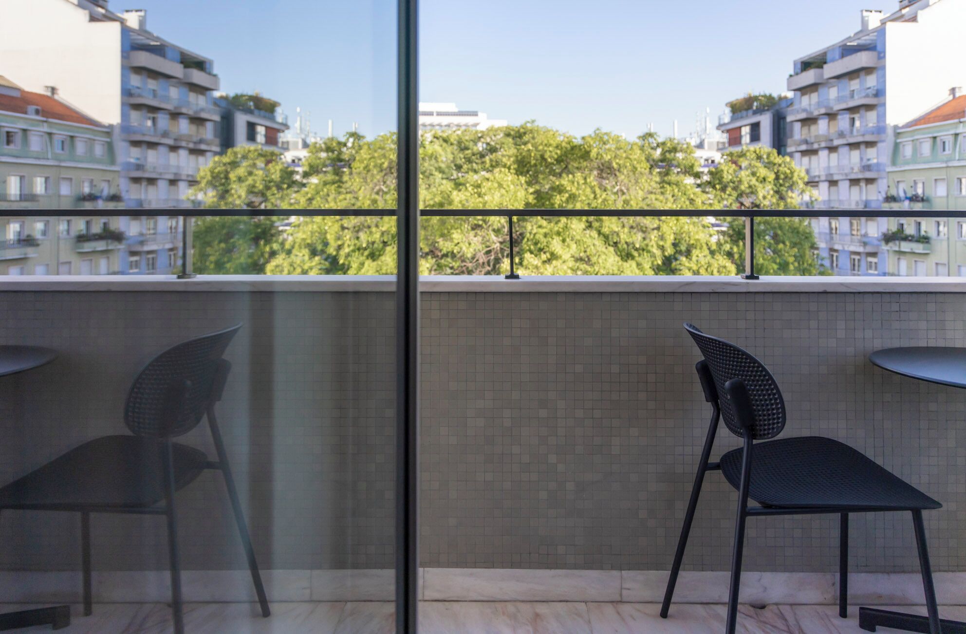 Un balcón con dos sillas y una mesa, con vistas a un paisaje urbano con edificios y árboles.