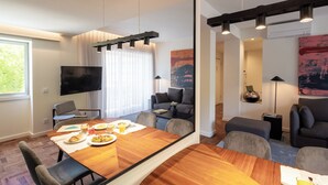 A modern living room with a wooden dining table, comfortable seating, a flat-screen TV, and artwork on the walls.
