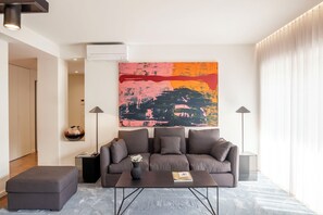 A modern living room with a gray sofa, a coffee table, and a large abstract painting on the wall. - 2-Bedroom Apartment in Avenidas Novas – Sophisticated Comfort in Central Lisbon (Lisboa)