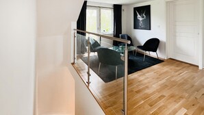 Un intérieur moderne avec un plancher en bois, une balustrade en verre et une vue sur un coin repas comprenant des chaises et une table.