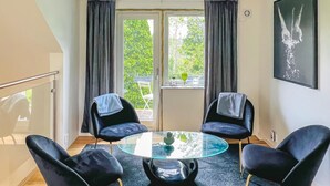 Une pièce moderne avec une table en verre entourée de quatre chaises noires, une fenêtre avec des rideaux, une petite table ornée d’objets décoratifs et une œuvre d’art encadrée accrochée au mur.