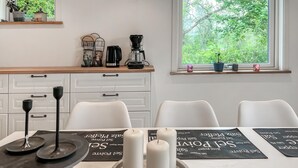 Une cuisine moderne avec des meubles blancs, une machine à café et une fenêtre donnant sur les arbres.