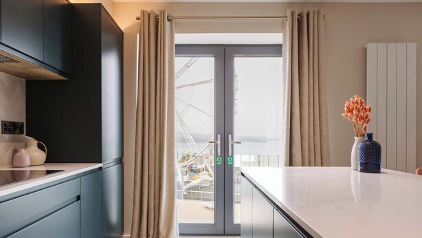 A modern kitchen with a large island, sliding doors to a balcony, and a view of a Ferris wheel. - Awaken your senses to The Amazon and leave feeling inspired & re-energised (Portrush)