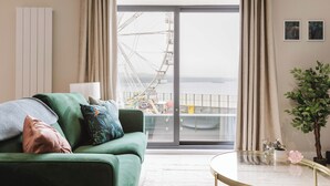 A modern living room with a green sofa, a glass coffee table, and a view of a Ferris wheel through a large sliding glass door. - Awaken your senses to The Amazon and leave feeling inspired & re-energised (Portrush)