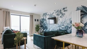 A modern living room with a green sofa, a dining table, and a large window. - Awaken your senses to The Amazon and leave feeling inspired & re-energised (Portrush)
