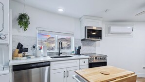 Une cuisine moderne avec des meubles blancs, des appareils en acier inoxydable, une table en bois et une fenêtre donnant sur les montagnes.