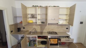 Eine kompakte Küche mit einer eingebauten Gaskochplatte, einem Spülbecken und offenen Regalen.
