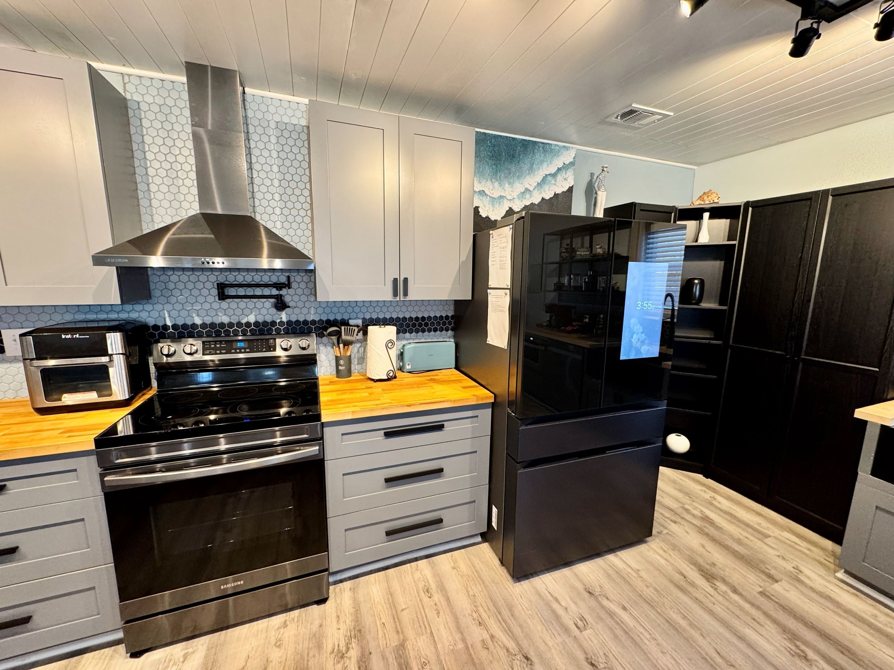 A modern kitchen with stainless steel appliances, grey cabinetry, and a wooden countertop.
