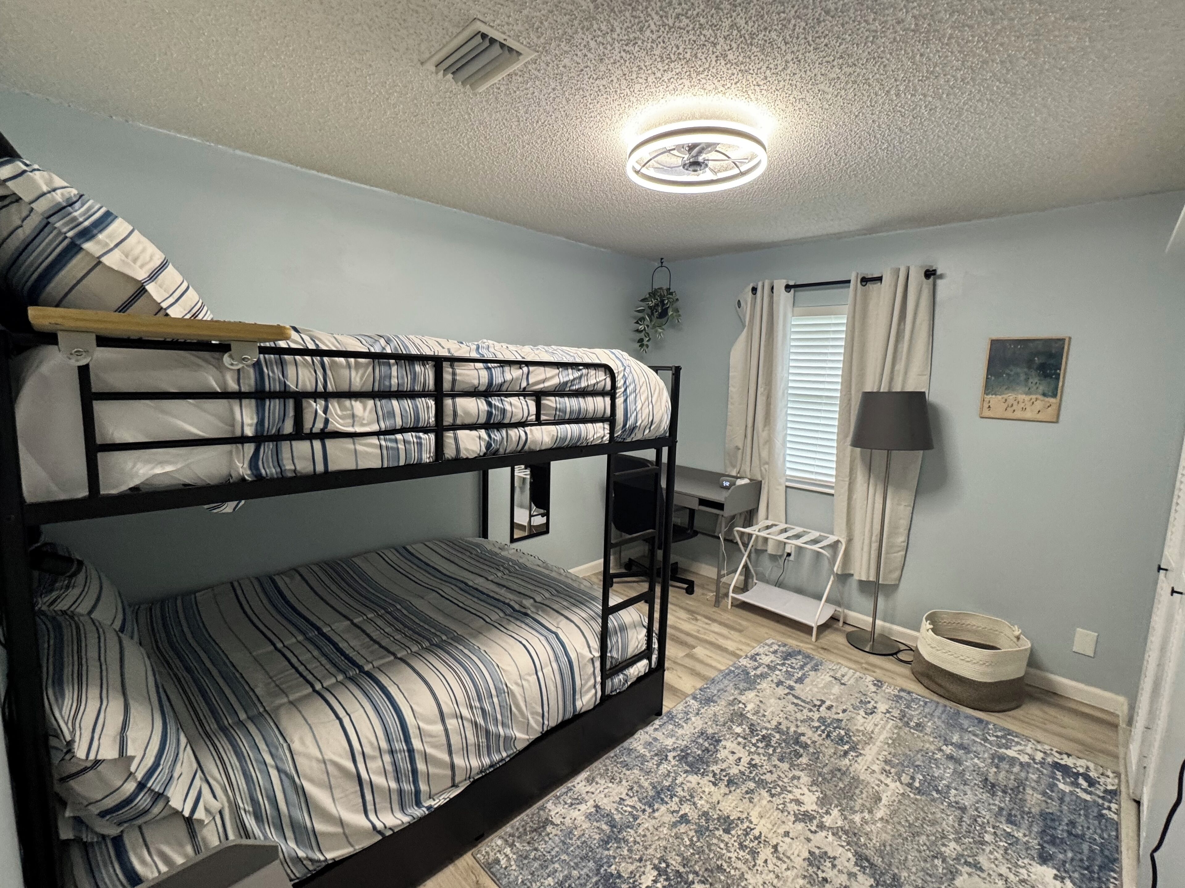 A bunk bed room with a desk, a lamp, and a small window with curtains.