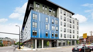 Un immeuble moderne à plusieurs étages, avec une façade aux couleurs variées, allant du bleu au blanc, de grandes fenêtres et une devanture bien visible, agrémentée d'une enseigne.