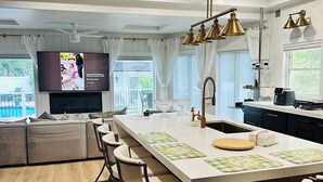 A modern kitchen with a central island, bar stools, and a flat-screen TV mounted above the island.