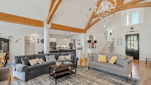 A spacious living area with a grey sofa, a smaller grey sofa, and a coffee table. There is a staircase leading to an upper level.