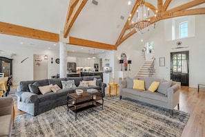 A spacious living area with a grey sofa, a smaller grey sofa, and a coffee table. There is a staircase leading to an upper level.