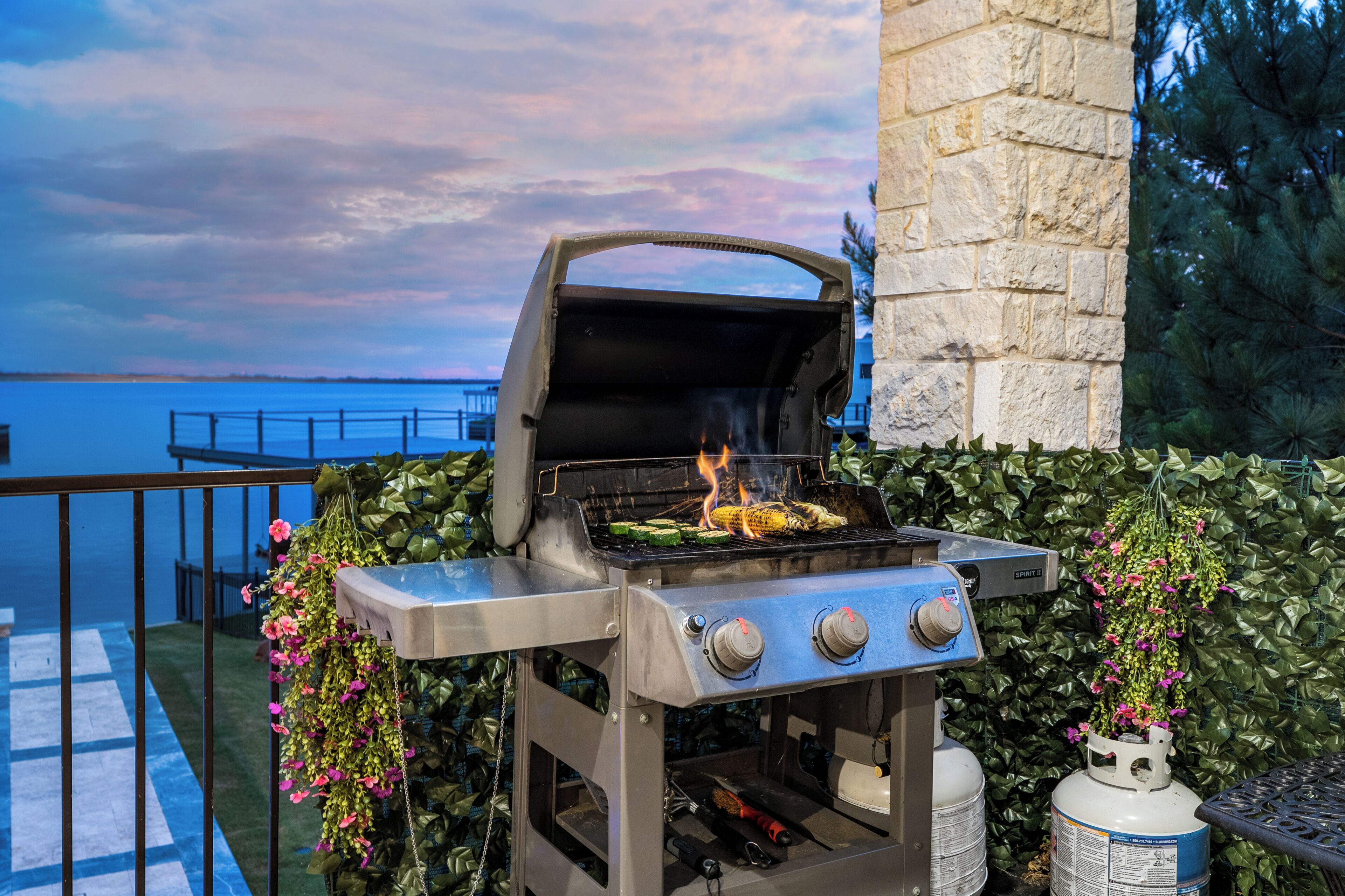An outdoor grill with a view of the water, a stone wall, and a metal railing.