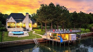 A house with a dock extending over a body of water, a swimming pool, and a well-maintained lawn.