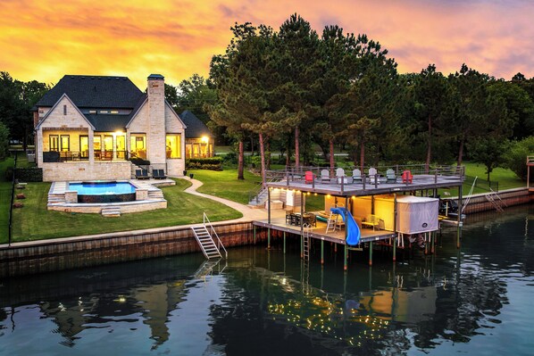 A house with a dock extending over a body of water, a swimming pool, and a well-maintained lawn.
