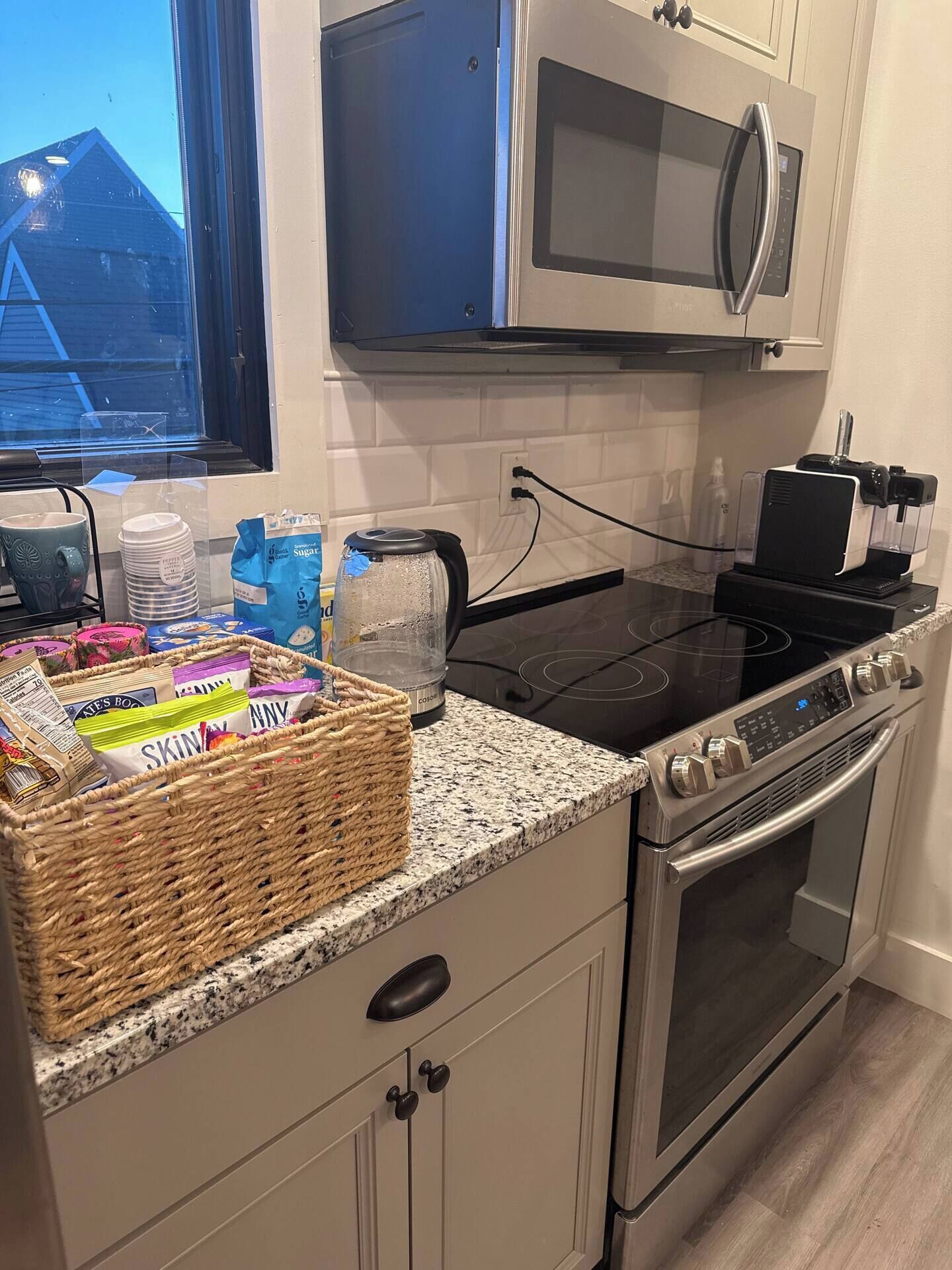 Een keuken met een magnetron, fornuis en oven. Op het aanrecht staat een mand met snacks en een fles water.
