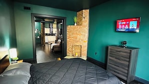 Un dormitorio moderno con una cama grande, un televisor montado en la pared y una pared de ladrillo decorativa.