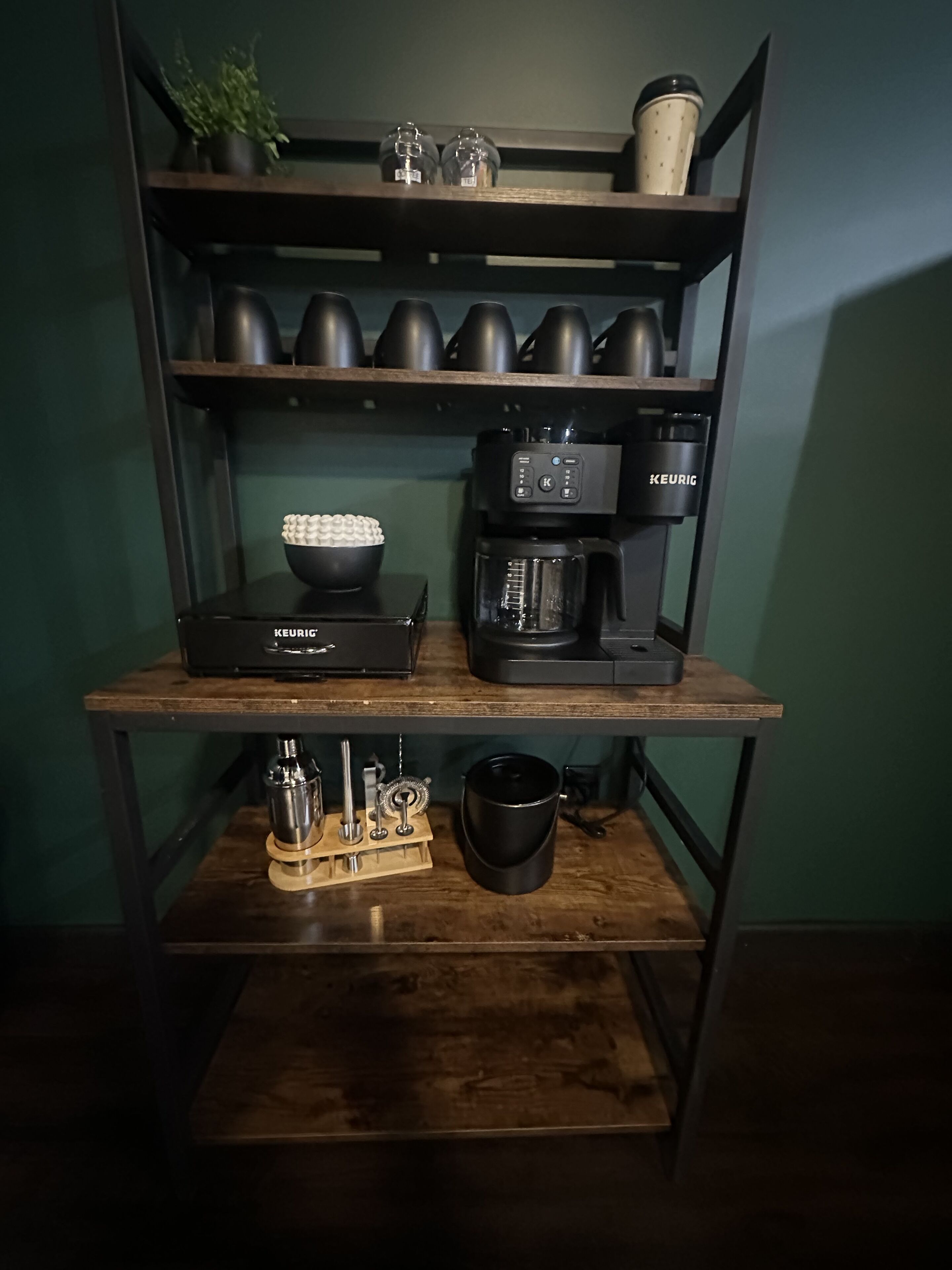 Un coin café équipé d’une machine Keurig, d’une cafetière et de divers accessoires pour préparer le café, le tout disposé sur une étagère en bois.