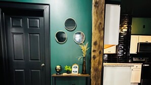 Un pasillo con piso de madera oscura, pared color verde azulado, puerta negra y una pequeña mesa con objetos decorativos.