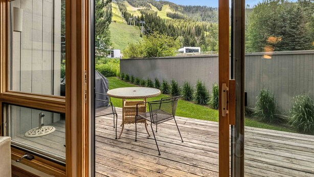 Une terrasse en bois avec une table ronde et des chaises, une vue sur un paysage vallonné et une clôture en bois.