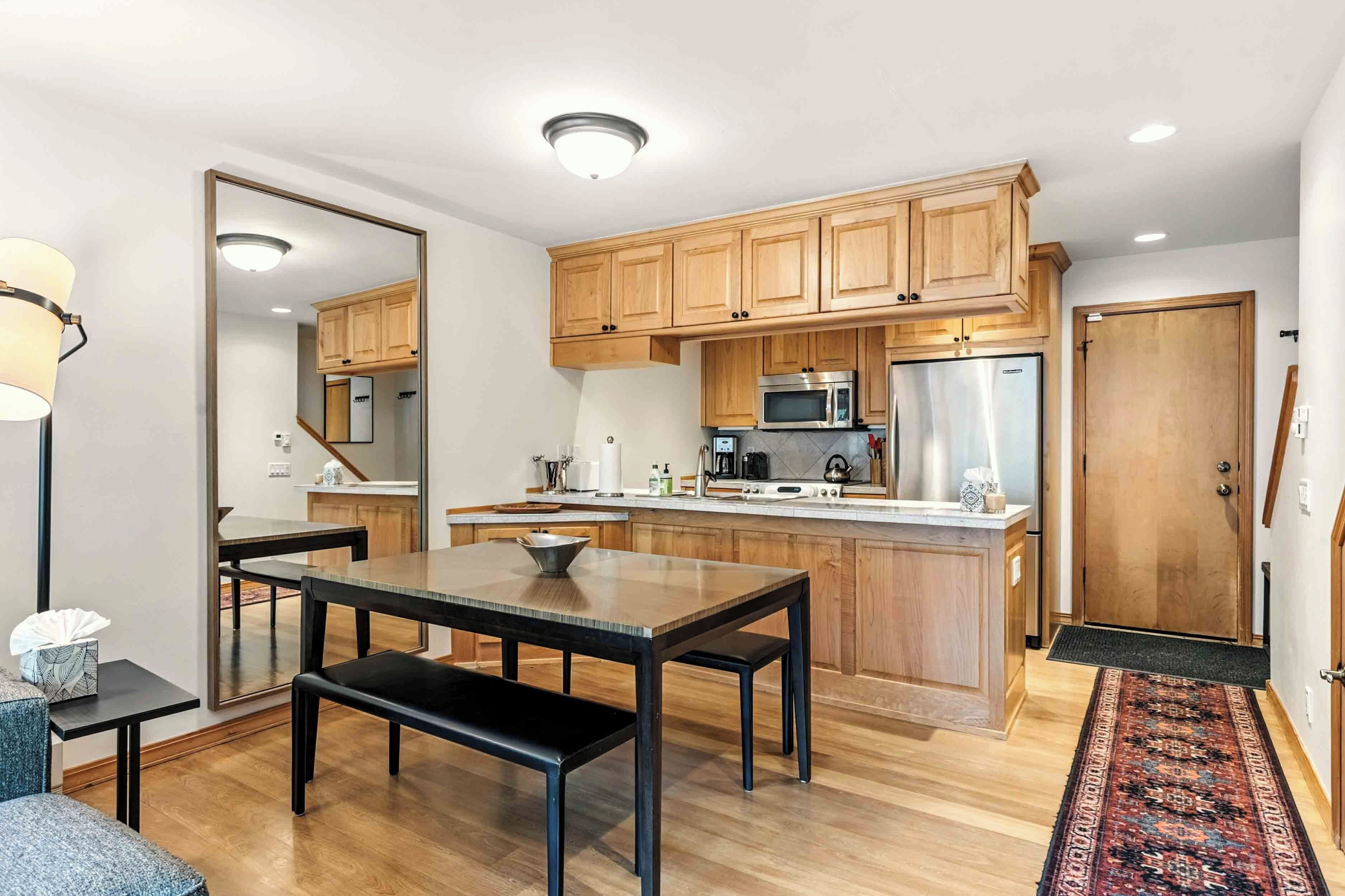 A modern kitchen with wooden cabinets, a central island, stainless steel appliances, and a dining area with a bench.