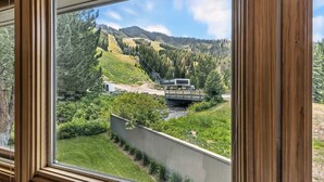Une vue à travers une fenêtre sur un paysage montagneux, avec un pont, de la végétation et un bâtiment.