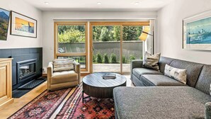 Un salon moderne avec une cheminée, un canapé, une table basse et une grande fenêtre donnant sur un paysage verdoyant.