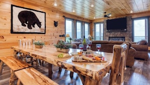 Un interior de madera con una mesa de comedor dispuesta para una comida, una chimenea y un televisor montado en la pared.