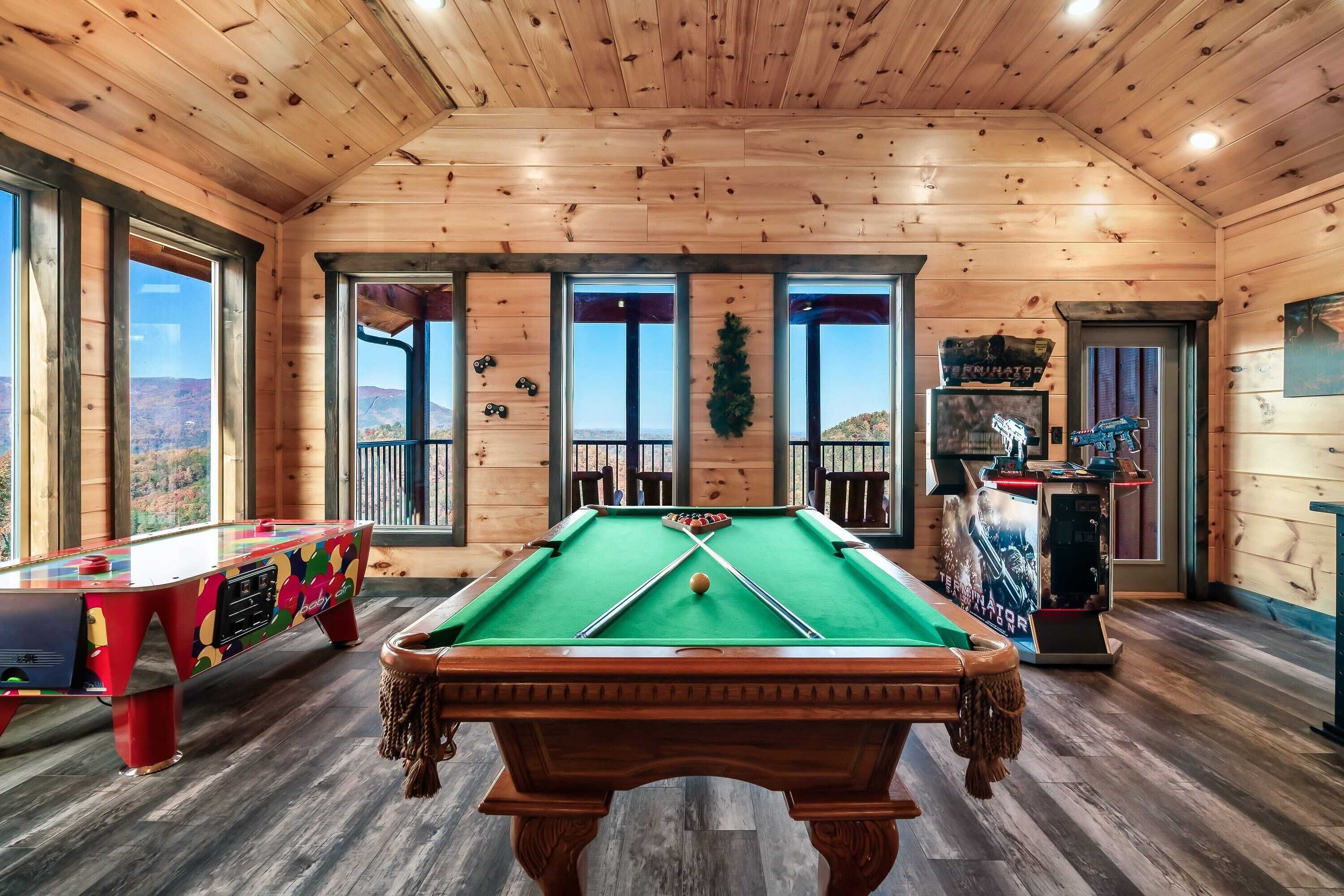 A wooden room with a pool table, a foosball table, and a billiards table.