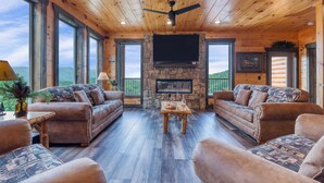 Interior acogedor de una cabaña con paredes de madera, una chimenea de piedra y ventanas amplias que ofrecen vistas panorámicas.