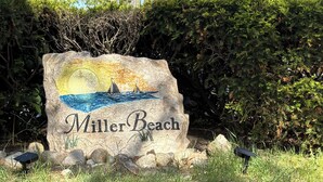 Un letrero de piedra con la inscripción 'Miller Beach', rodeado de césped y rocas.