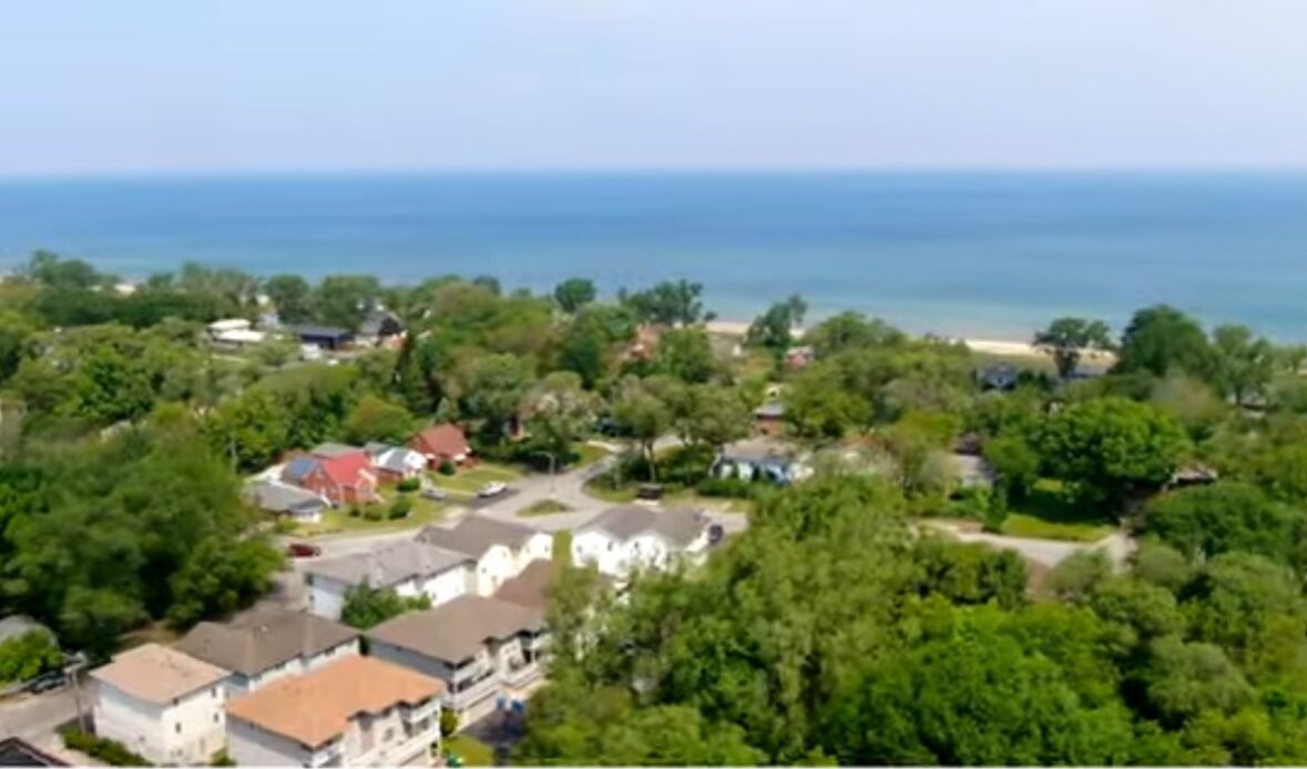 An aerial view of a residential area with houses, greenery, and a coastline.
