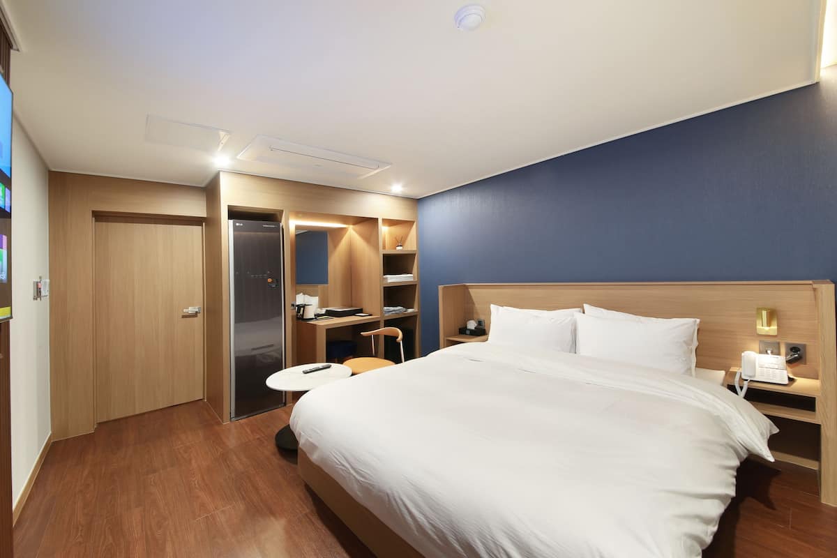 A hotel room with a bed, bedside table, nightstand, wardrobe, and a TV screen displaying a news channel.