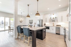 Une cuisine moderne dotée d’un îlot central, de luminaires suspendus et offrant une vue sur l’extérieur.