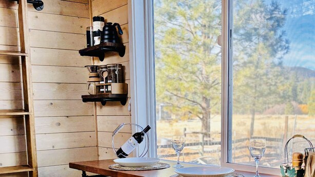 A wooden interior with a dining table, two bar stools, a wine rack, and a large window offering a view of trees. - Couple’s retreat in Tiny Home w soaking tub/beach at Upper Lake (Upper Lake)