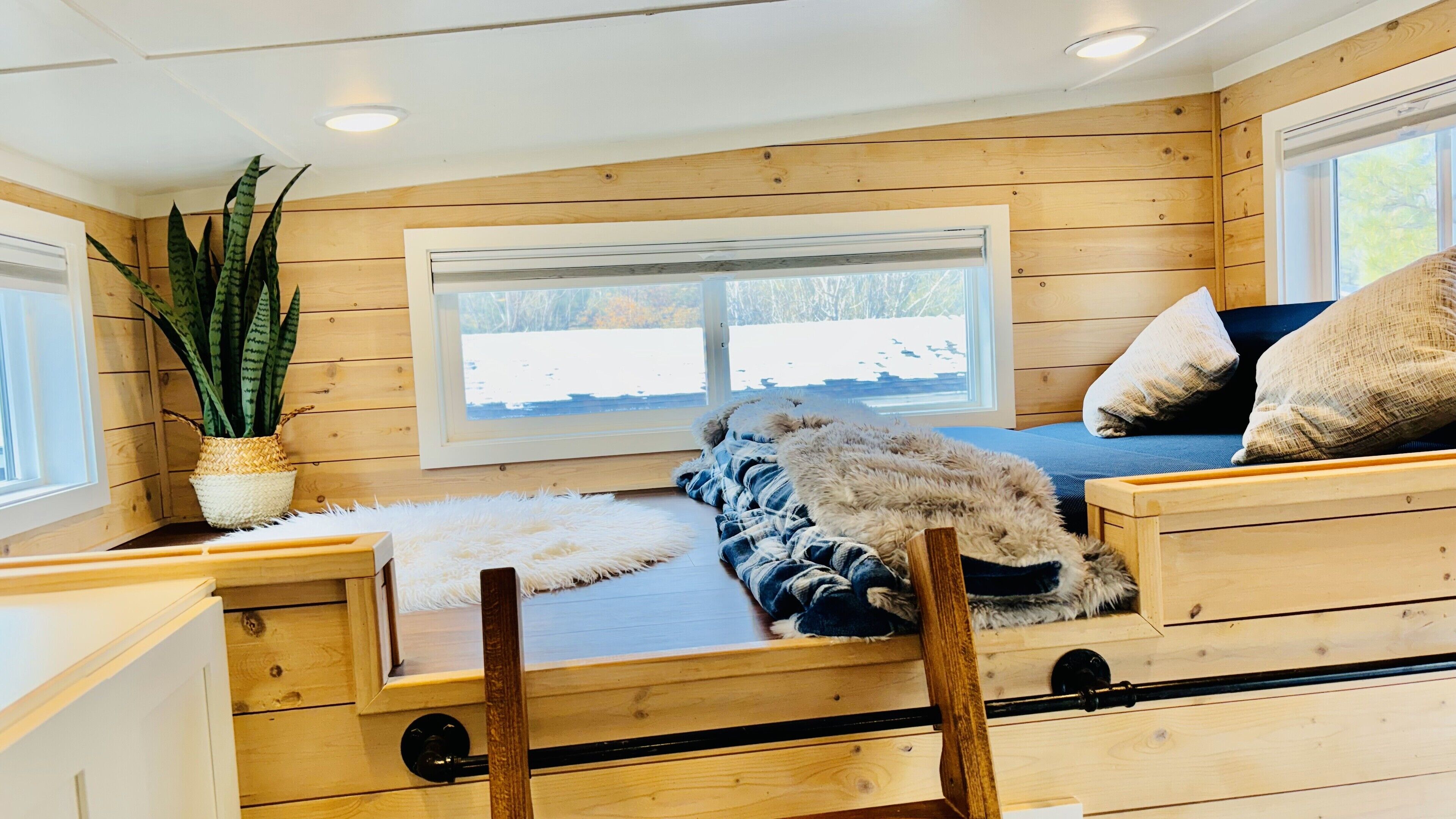A cozy cabin interior with a wooden bed, a window with a view of a snowy landscape, and a potted plant.