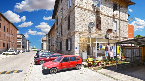 A stone building with a shop on the ground floor, parked cars, and a clear blue sky. - Apartment 2396/160471 (Istria - Pula), 110m from the beach (Pula)