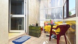 A small, enclosed patio area with a sliding glass door, a table with yellow cushions, and a chair. There are green storage boxes and a blue rug on the floor. - Apartment 2396/160471 (Istria - Pula), 110m from the beach (Pula)