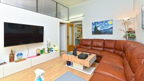 A modern living room with a leather sofa, a flat-screen TV, a wooden coffee table, and a painting of a night sky. - Apartment 2396/160471 (Istria - Pula), 110m from the beach (Pula)