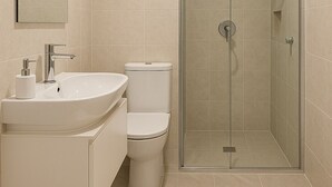 Ett modernt badrum med en dusch som är avskärmad med glasväggar, ett vitt handfat och en toalett.