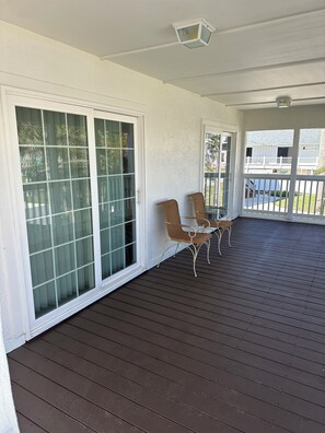A covered porch with a wooden floor, two wicker chairs, and a sliding glass door. - Hammock Beach Cottage (Palm Coast)