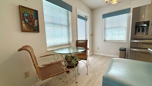 A dining area with a glass table, wicker chairs, and a blue bench. There are windows with blinds, a chandelier, and a stainless steel oven. - Hammock Beach Cottage (Palm Coast)