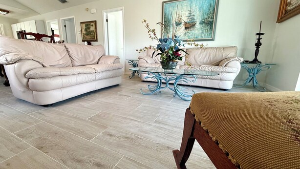 A spacious living room with two beige leather sofas, a glass coffee table, and a wooden bench. - Hammock Beach Cottage (Palm Coast)
