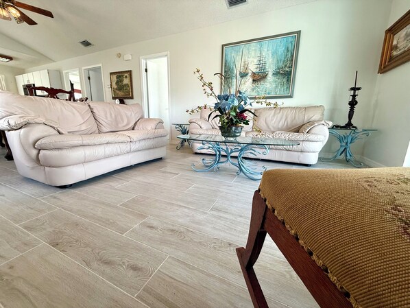 A spacious living room with two beige leather sofas, a glass coffee table, and a wooden bench.