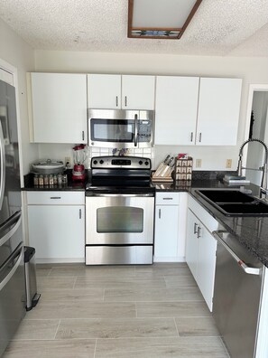 A modern kitchen with stainless steel appliances, white cabinetry, and a herringbone-patterned backsplash. - Hammock Beach Cottage (Palm Coast)